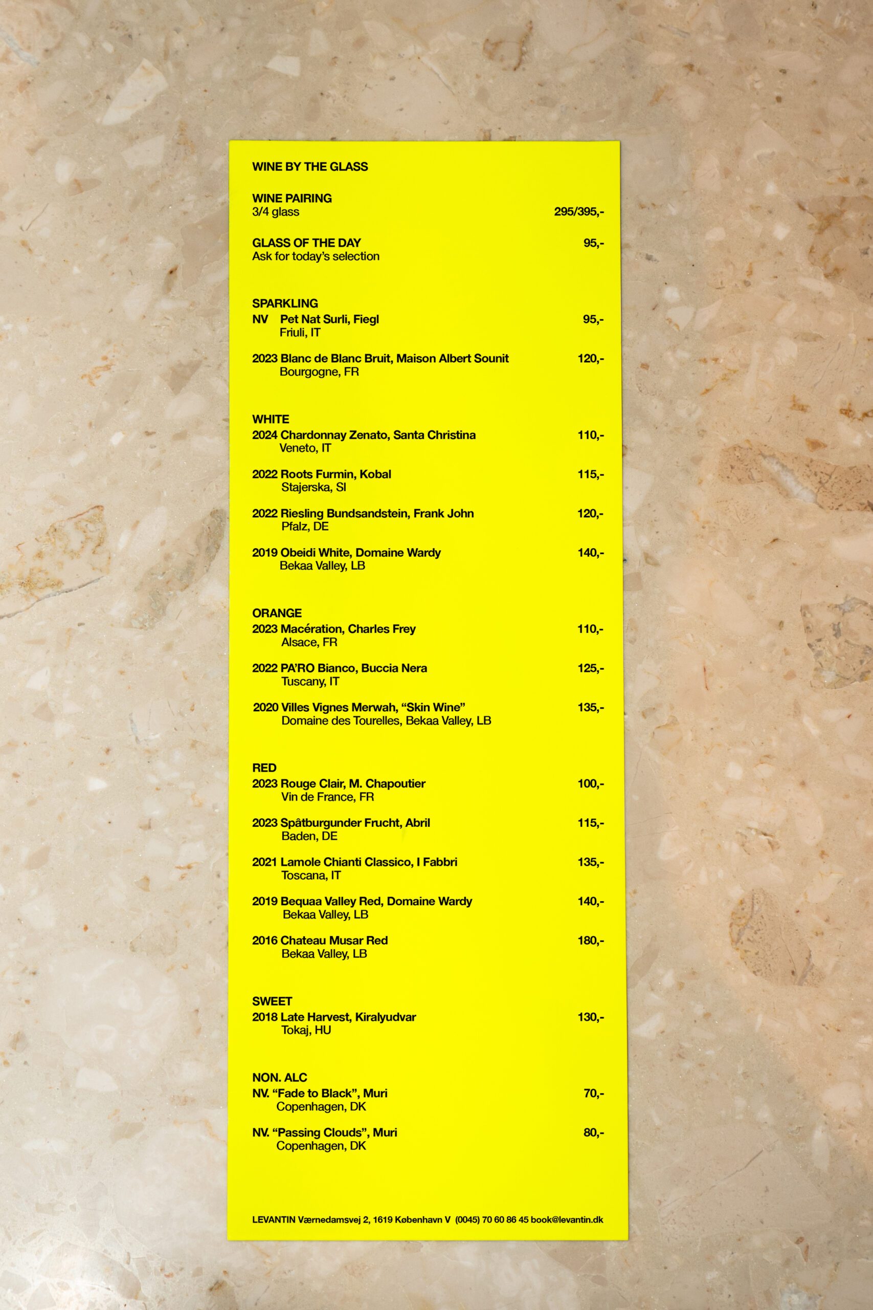 List of wines on glass at Levantin. Yellow paper menu placed on a patterned wallpaper.